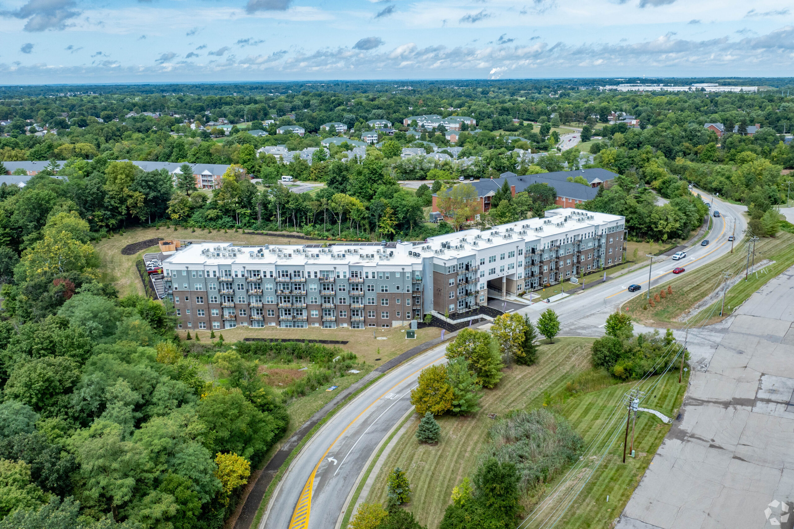 Aerial view of Florence Hall's modern apartment buildings surrounded by greenery, with a winding road and scattered vehicles leading to the entrance.
